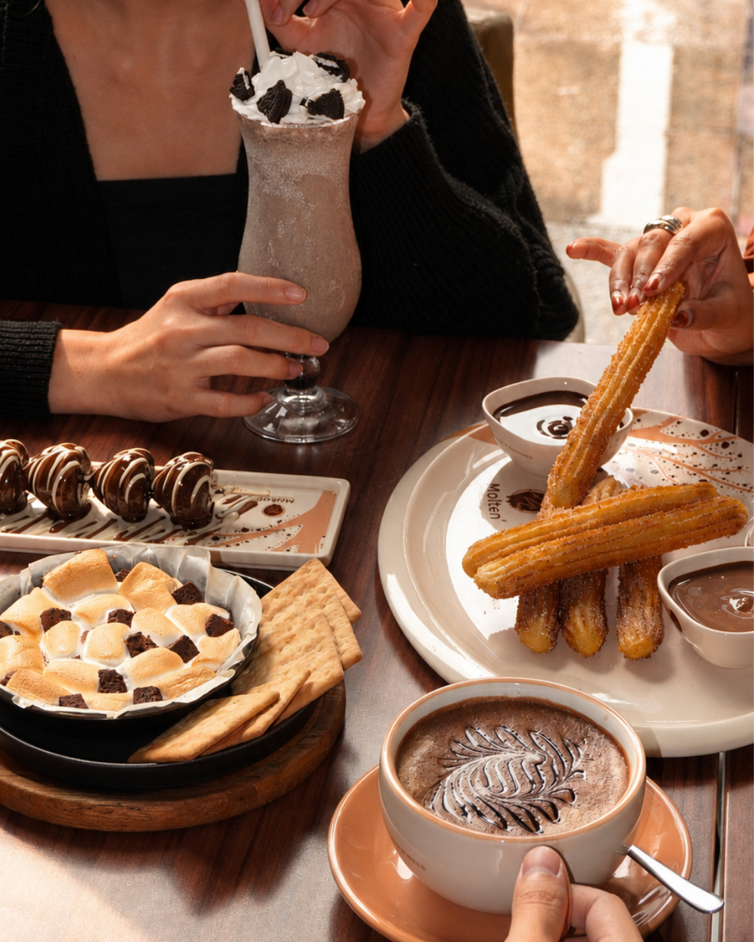 A cafe table with a milkshake, churros with dips, a s'mores skillet, chocolate-dipped treats and a hot chocolate (slide 4 of 4)